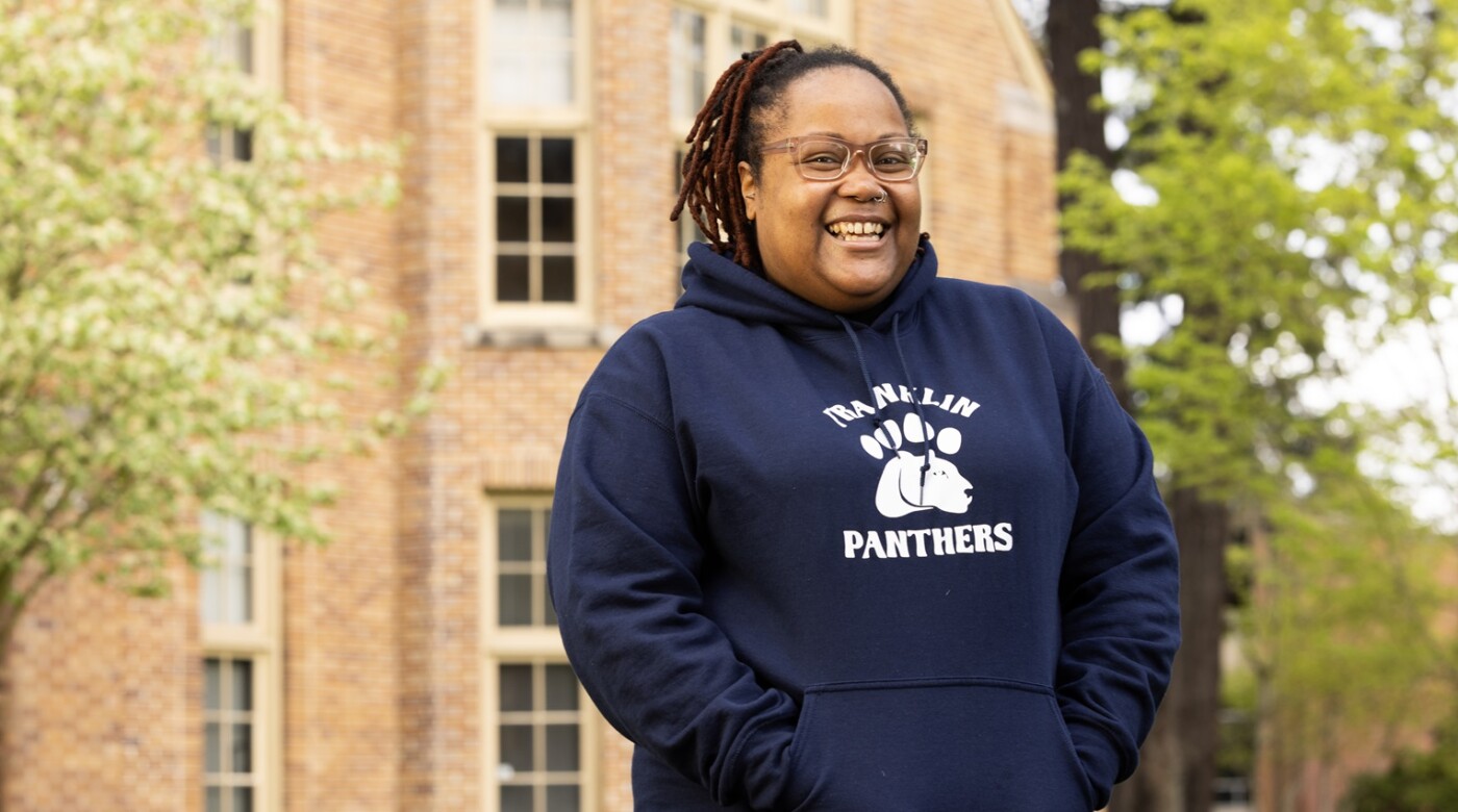 Zoneice Grose smiles for the camera outside on PLU's campus on a spring day. She's wearing a dark blue hoodie that reads 'Franklin Panthers'.