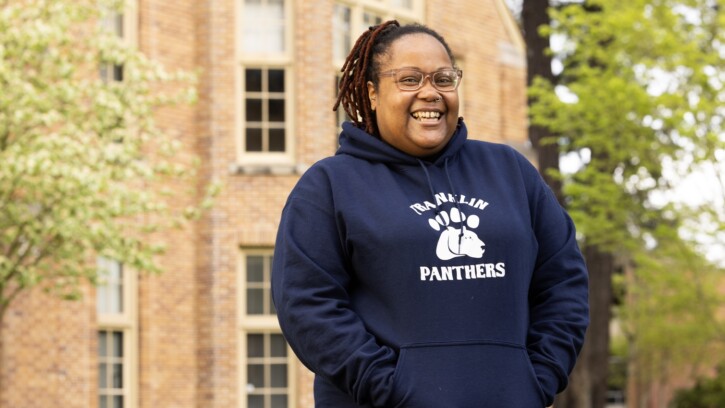 Zoneice Grose smiles for the camera outside on PLU's campus on a spring day. She's wearing a dark blue hoodie that reads 'Franklin Panthers'.