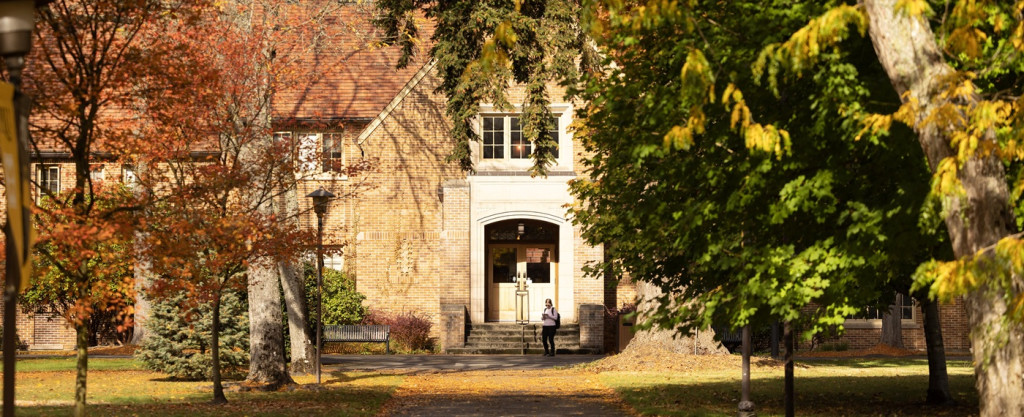 Web Banner - Xavier in Fall On a sunny fall day on campus, a student wearing a backpack walks outside of the light brick Xavier academic building.