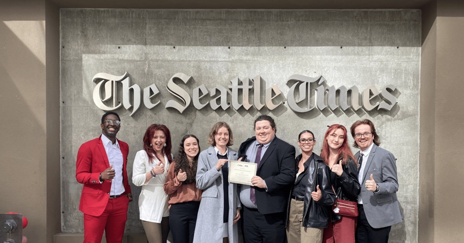 Students from PLU's 'The Mast' student newspaper smile and pose in front of 'The Seattle Times' large sign