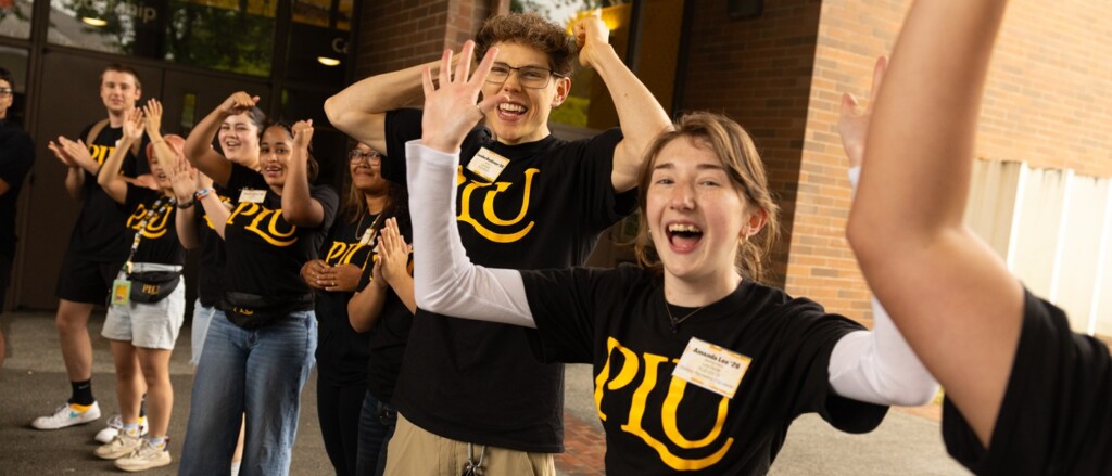PLU students wearing black t-shirts with the yellow PLU logo cheer as new students enter the building for Convocation.