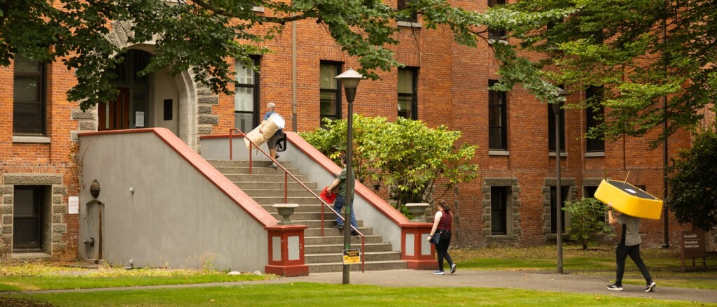 First-year students and their families walk to the front steps of the red brick Harstad Residence Hall.