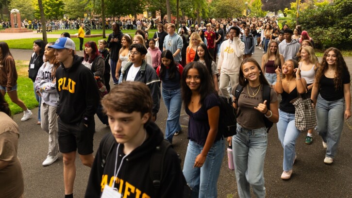 A group of new PLU students smile at the camera as they walk together through campus to PLU's Convocation ceremony, an annual PLU tradition.