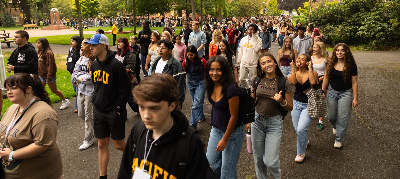 A group of new PLU students smile at the camera as they walk together through campus to PLU's Convocation ceremony, an annual PLU tradition.