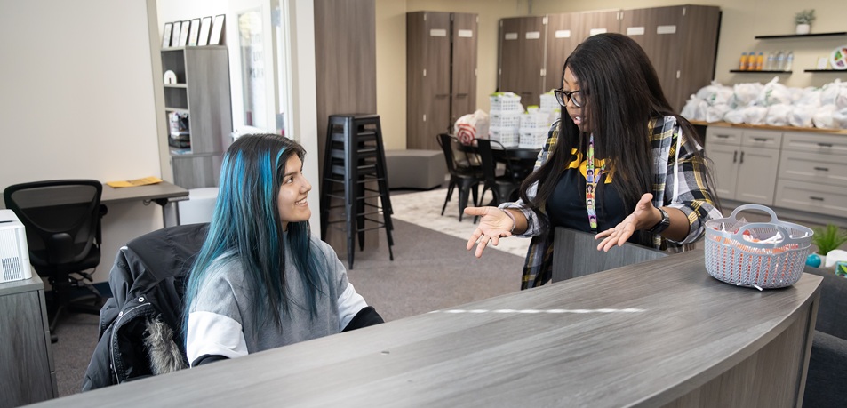 A PLU student sitting at a desk chats with a teacher during her social work internship at a local middle school.