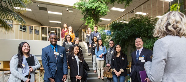 Students in professional attire and wearing nametags stand on stairs listening to a speaker during a visit to Amazon headquarters in Seattle.