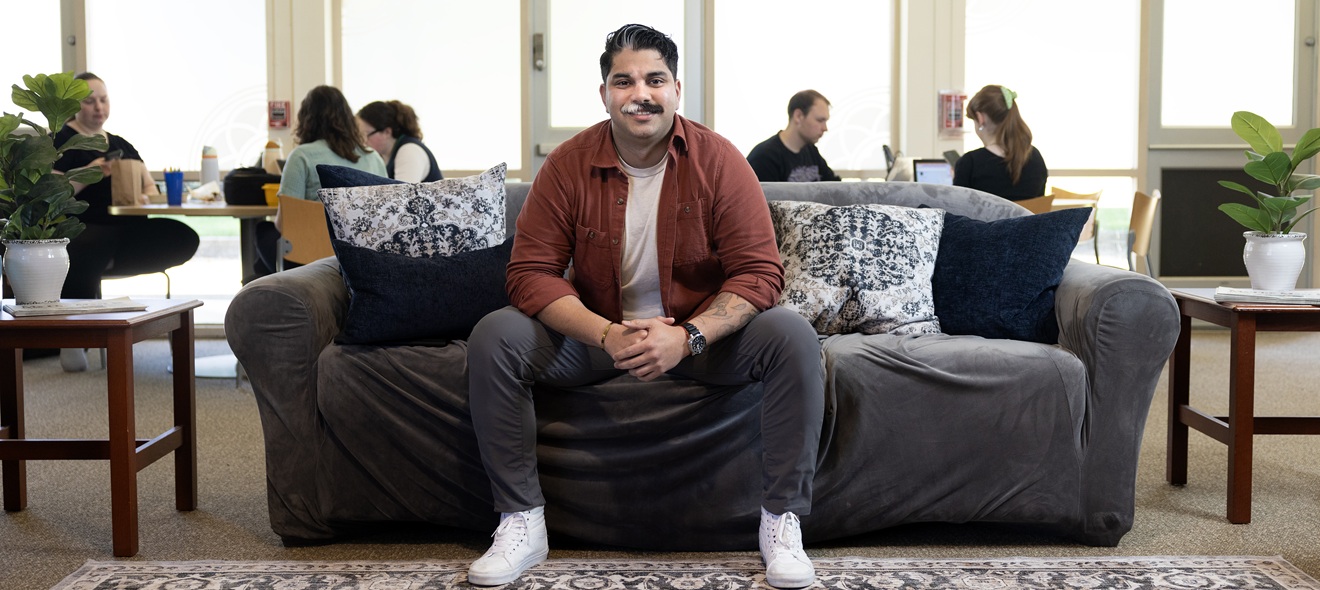 Adrian sits on a couch in the lounge of PLU's Wellbeing Services and Resources space on campus
