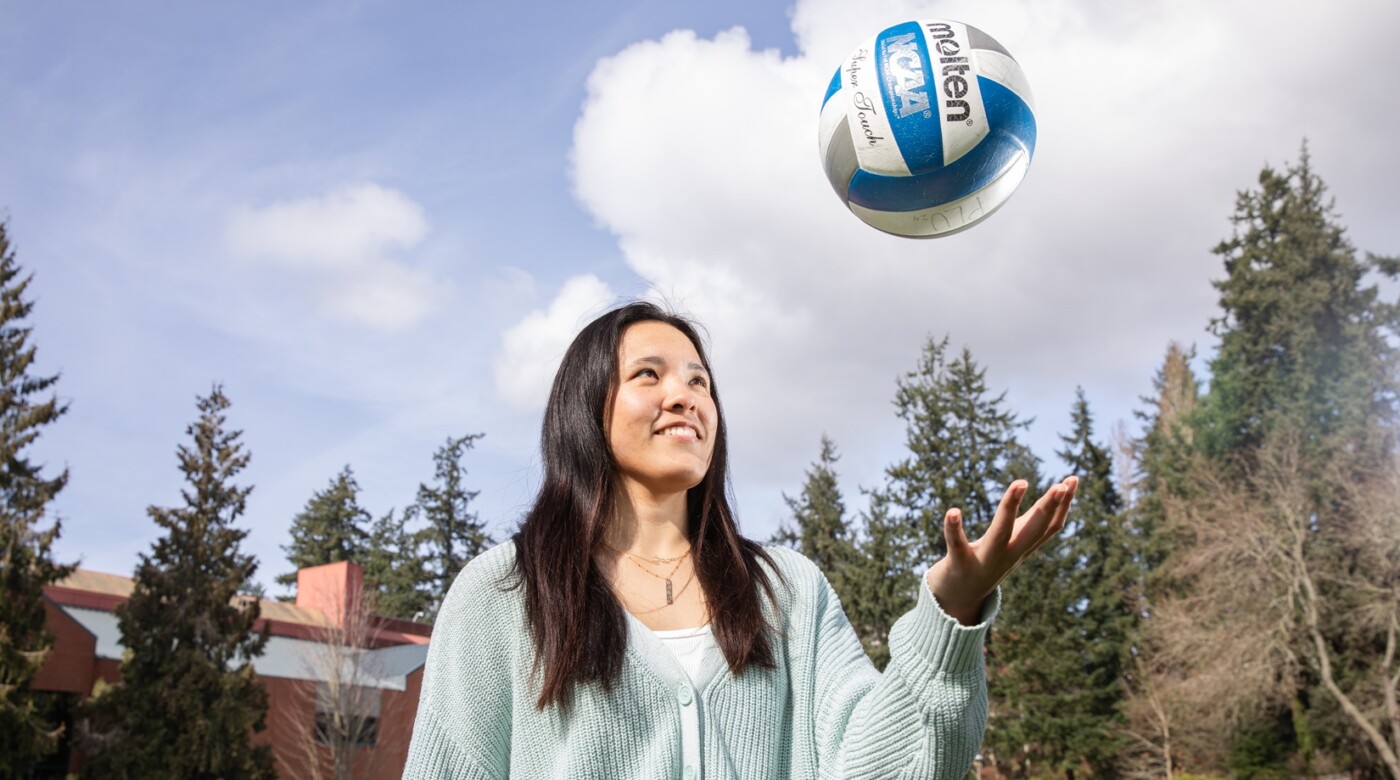 Haley Goto tosses a volleyball outdoors with trees and a brick building behind