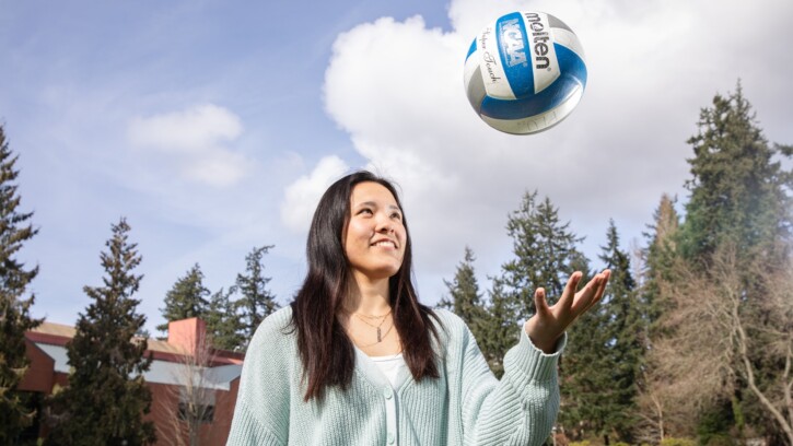 Haley Goto tosses a volleyball outdoors with trees and a brick building behind