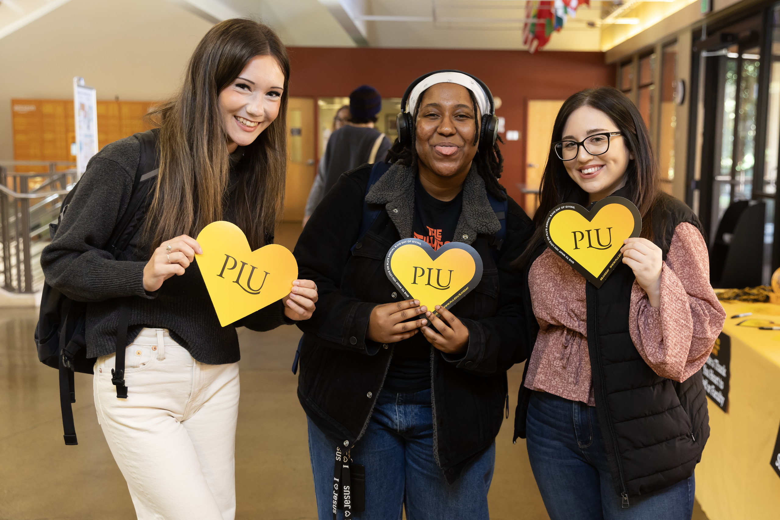 Three students hold Bjug Day hearts and smile into the camera