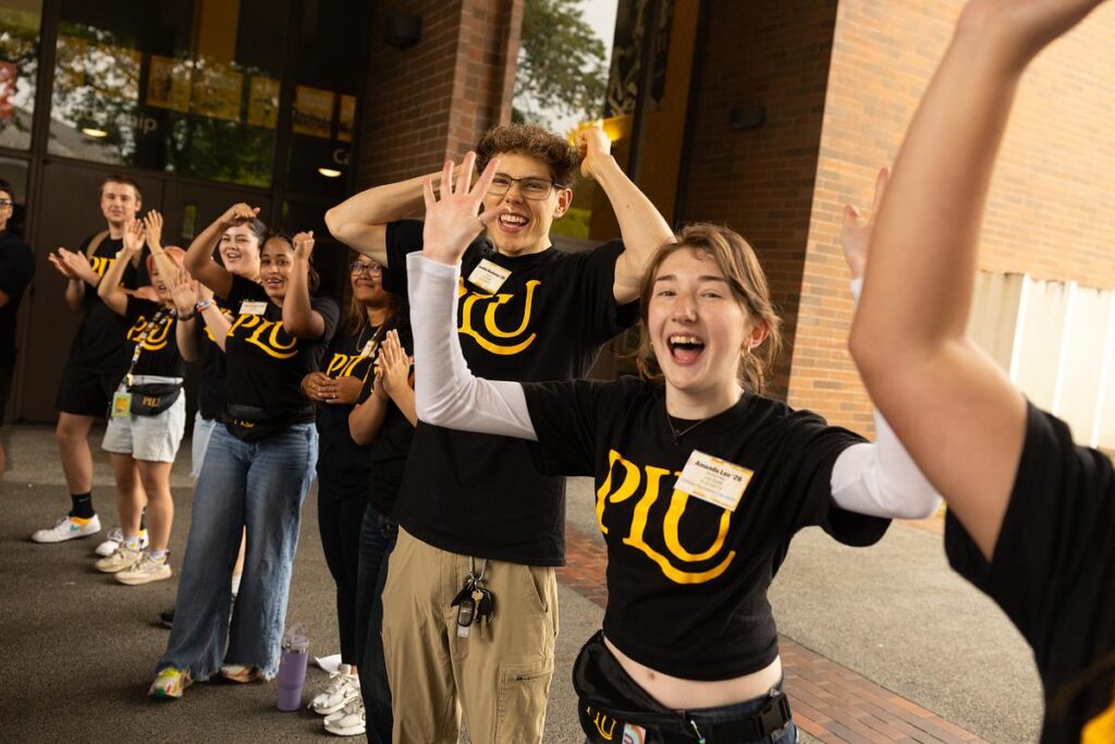 Students stand outside cheering with their hands in the air