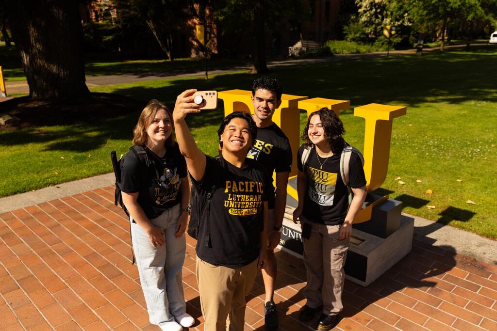 Photo of students wearing PLU gear, outside taking a group selfie.