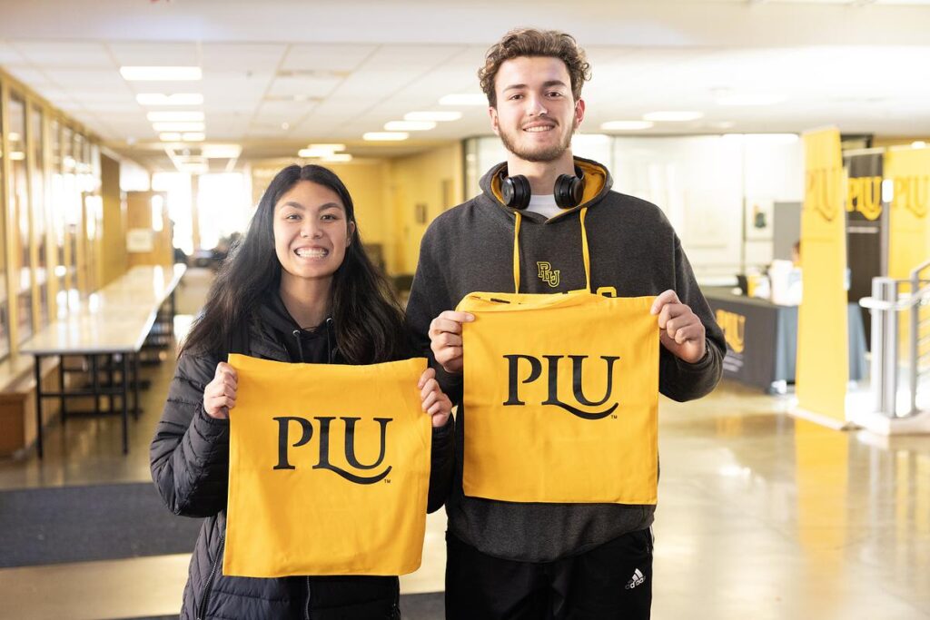 Two students holding up PLU signs and smiling at the camera.