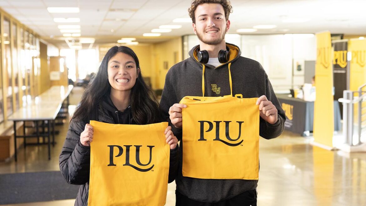 Two students holding up PLU signs and smiling at the camera.