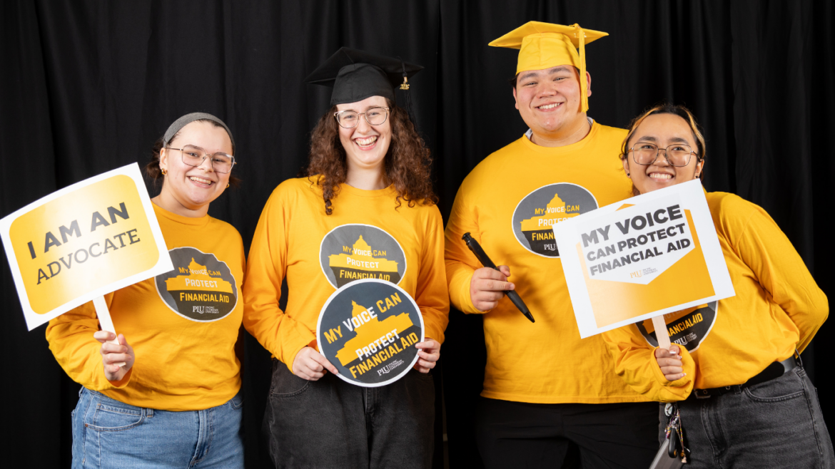 Four students hold signs and look into the camera and smile