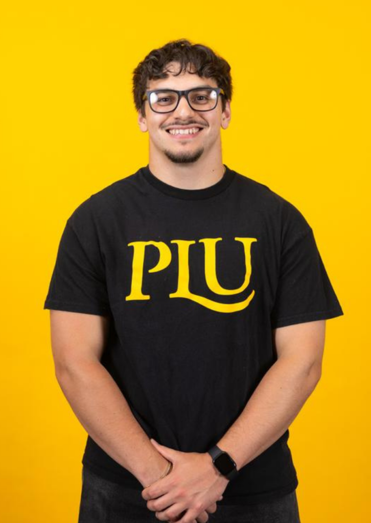 Young man in PLU t-shirt smiling against yellow background