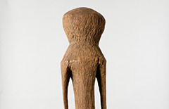 This Moba figure, in an abstract human form is carved from a single piece of wood. It shares common characteristics of other medium-sized Moba figures including elongated arms, short legs, and bulbous shaped head. It shows sign of wear on the wood such as some chipping on the arms, a hole on tope of the head, a cracking of the wood on the left side, and some wood deterioration, which suggests that this figure was outside and used by the society.