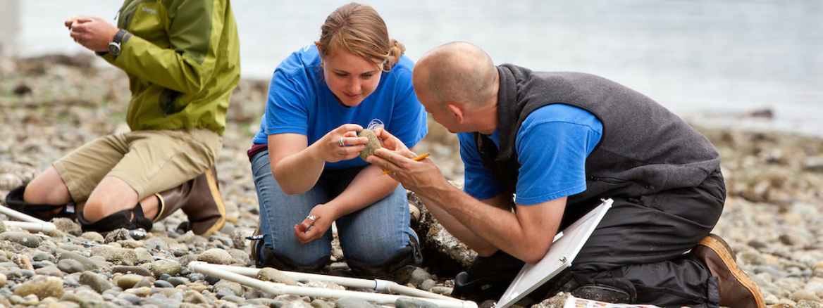 A student and faculty member looking at a specimen on the beach