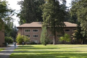 Exterior image of Hong Hall at Pacific Lutheran University. Brick building, surrounded by lush greenery and trees.