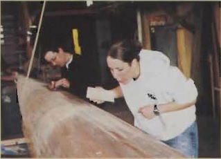 The crew teams restores a wooden boat named for longtime supporter Marjorie Anderson. Pictured, Heather Short (’04) and Katie Schlepp (’05) sand the wooden shell.