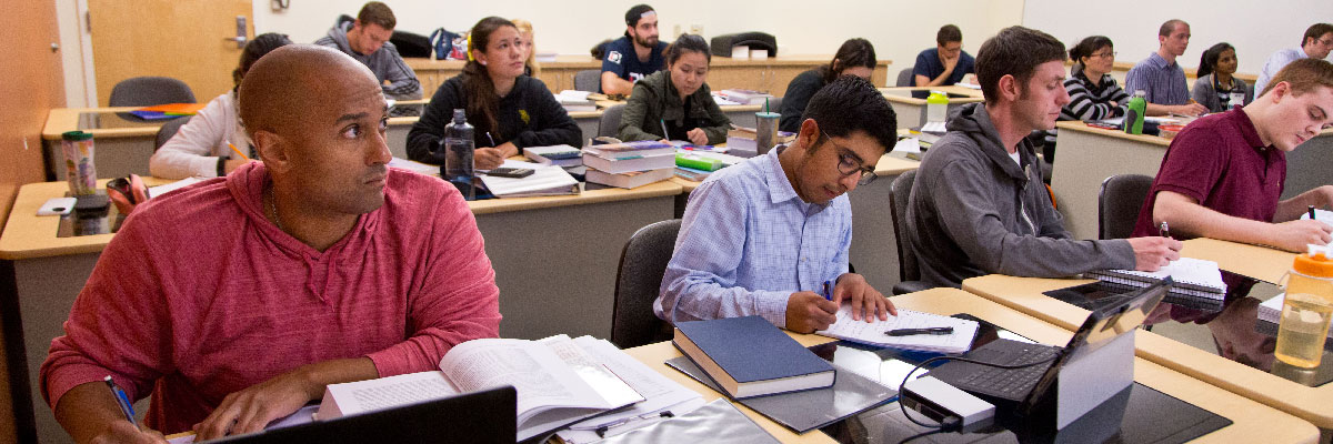 Students in a classroom taking notes while listening to professor Students in a classroom taking notes while listening to professor