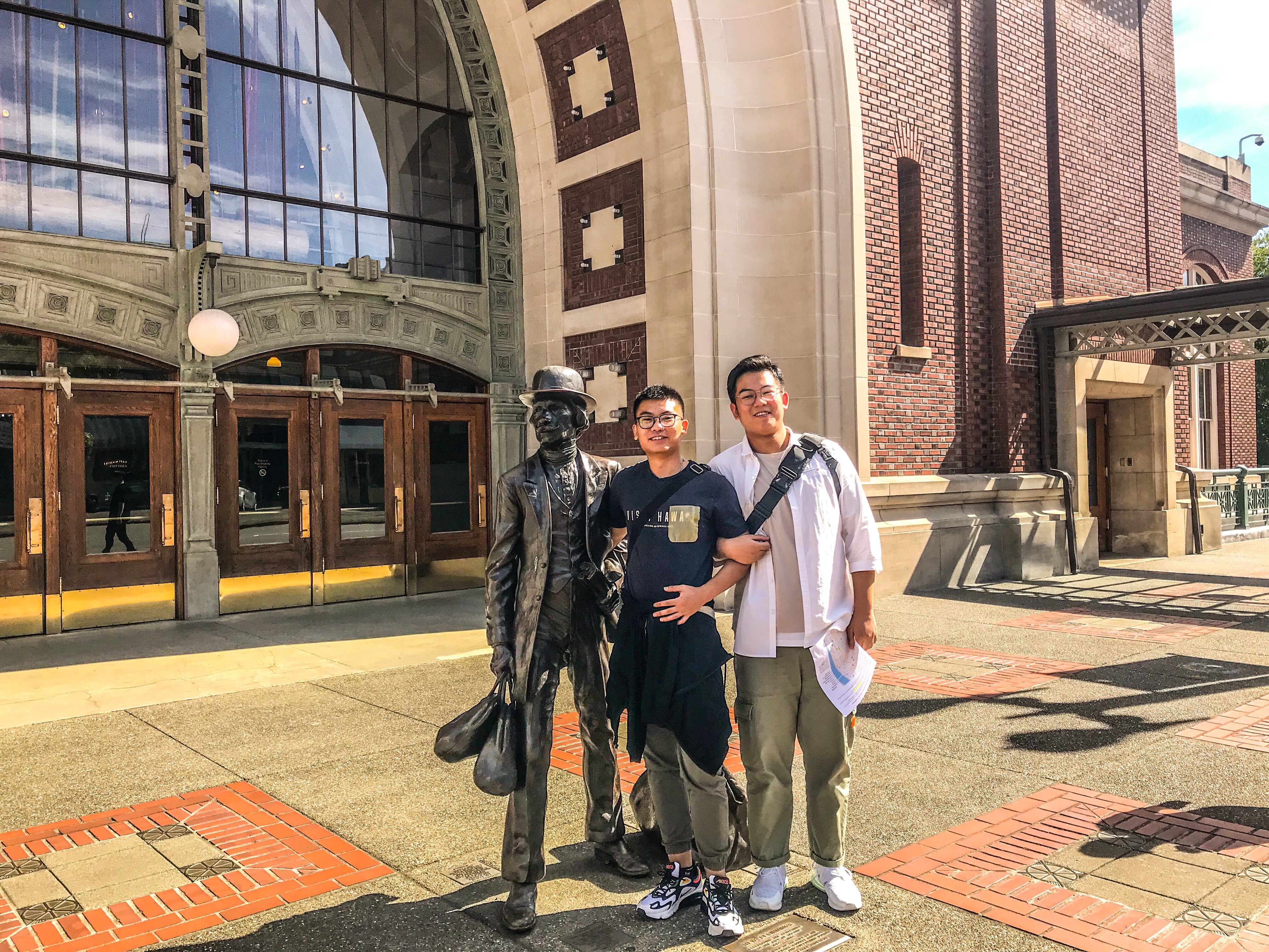 Two Chinese students stand arm-in-arm with a statue in Downtown Tacoma