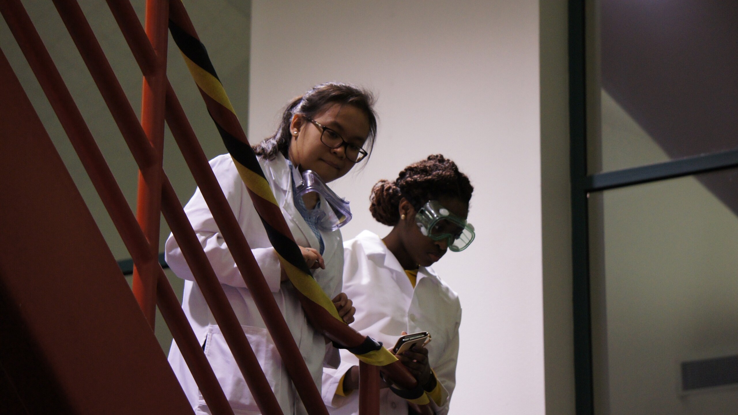 2 students in lab coats standing on the stairs