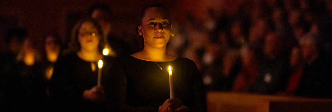 Several women walking while holding candles in a darkly lit venue.