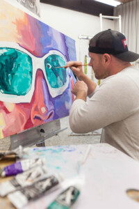 Student oil painting a colorful face with sunglasses