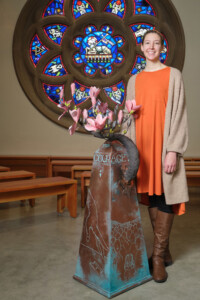 A student stands next to her three-dimensional mixed media sculpture on display in the PLU Chapel