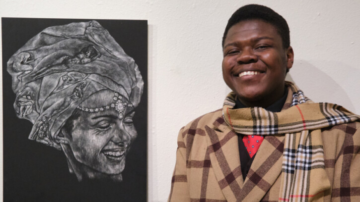 Art & Design student Isaiah stands next to his award winning artwork with a big smile on his face