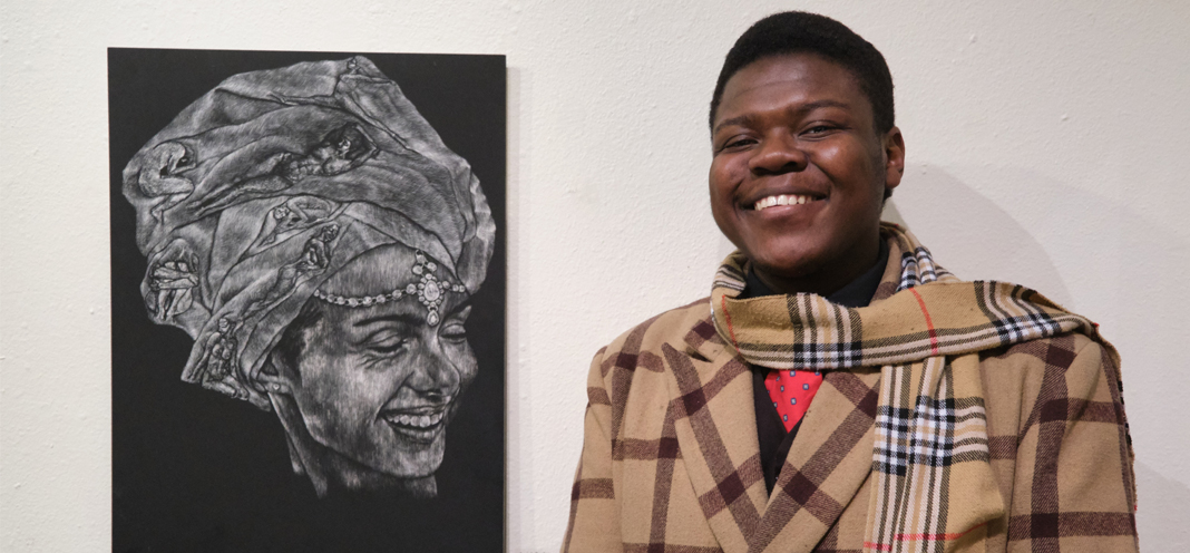 Art & Design student Isaiah stands next to his award winning artwork with a big smile on his face