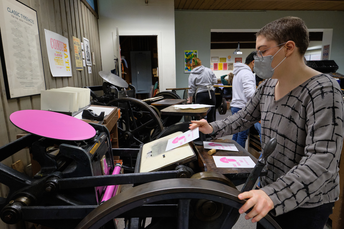 Student operating a platen press with bright pink ink.