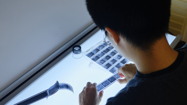 A student examines photography film negatives at a light table.