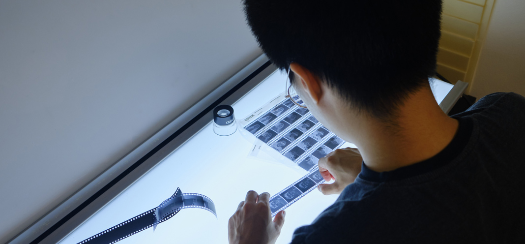 A student examines photography film negatives at a light table.