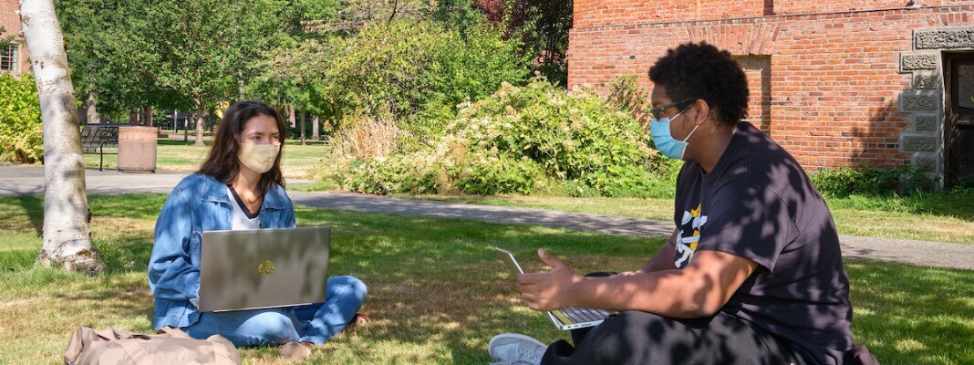 Two students studying on the lawn with masks