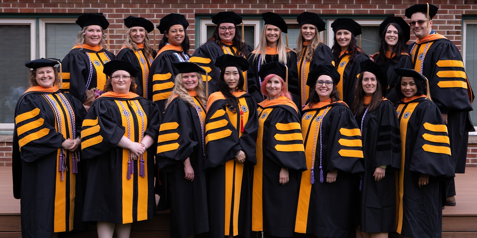 Web Banner - DNP 04 A group of DNP graduates in their black and yellow graduation robes and doctorate caps stand together outside for a group photo.