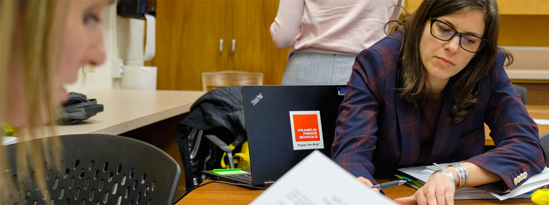 Two PLU student work together while sitting at a table reviewing paperwork. One student has dark hair and glasses the other is blond.