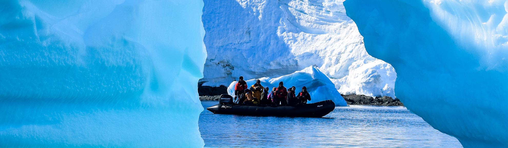 Several people on a boat, on the waters in Antarctica. Seen through two large chunks of ice.