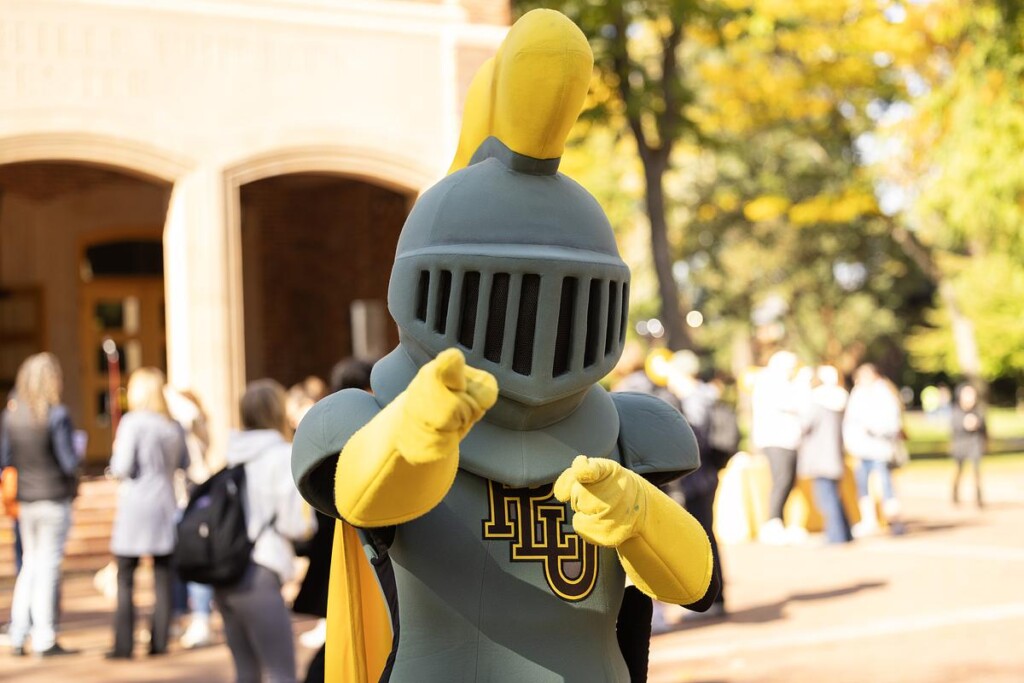 Armored knight mascot with yellow accents, posing outdoors.