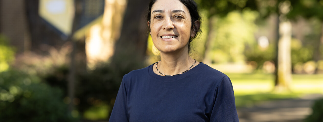 Woman in navy shirt smiling outdoors on campus grounds
