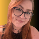 Headshot of Kelli Cook wearing black glasses and a black top, with long reddish-brown hair, smiling at the camera against a gold and black background.