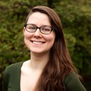 A brunette woman with glasses faces the camera with a smile.