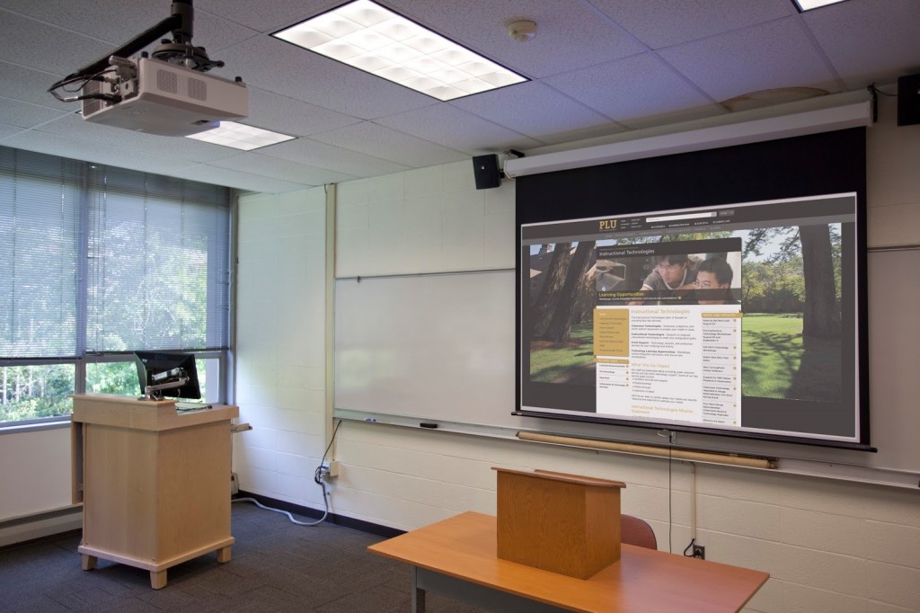 A classroom in the Admin building, with a large projector screen hanging in front of the white board.