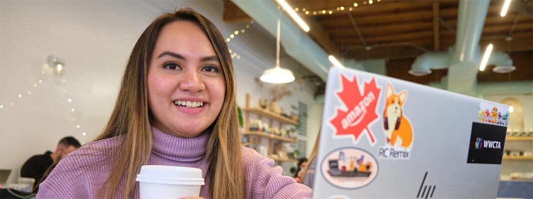 April Rose Nguyen holding a coffee cup while sitting in front of her computer