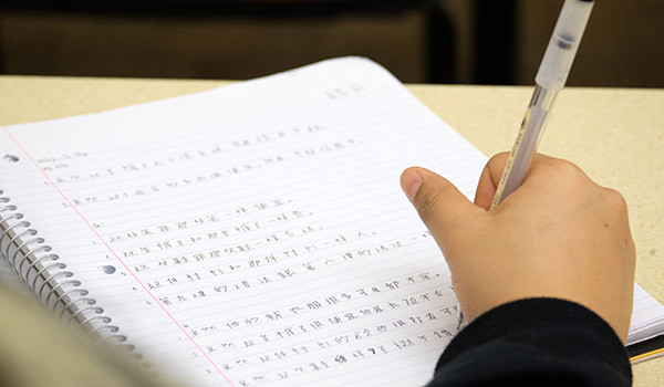 A student holding a pen and writing Chinese characters on a journal