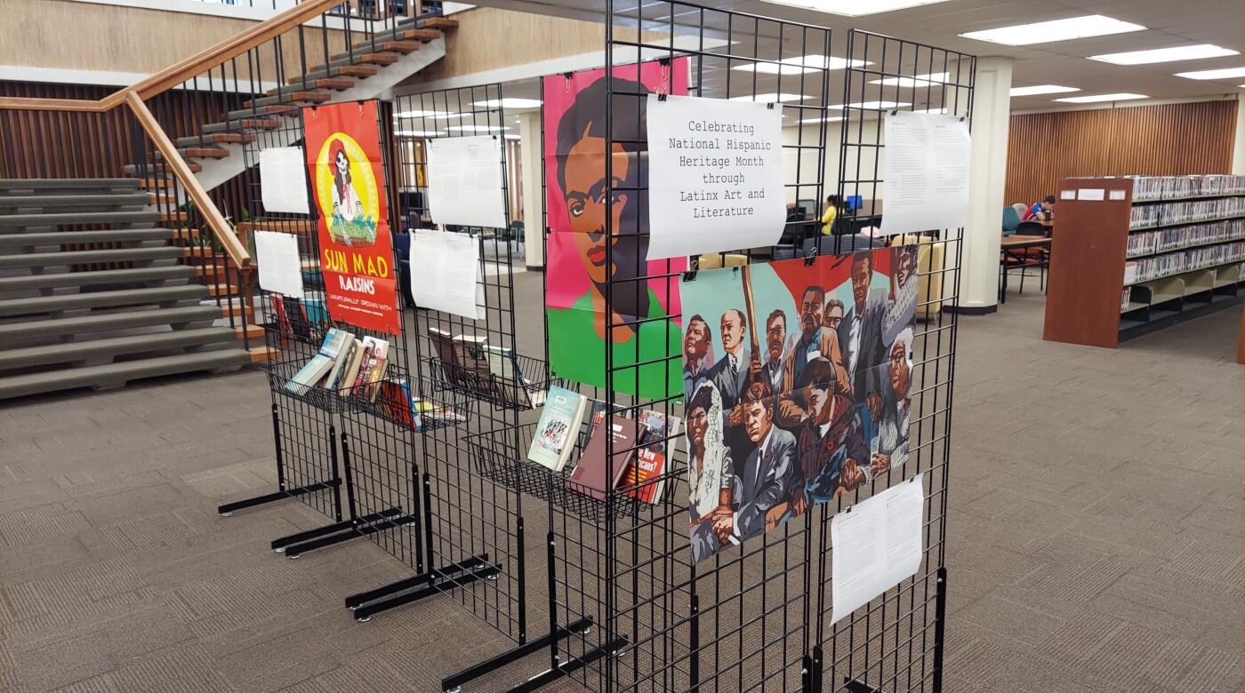 Black wire displays holding a number of poster and books stand in the middle of a library lobby.