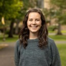Young woman smiling outdoors in gray sweater at park