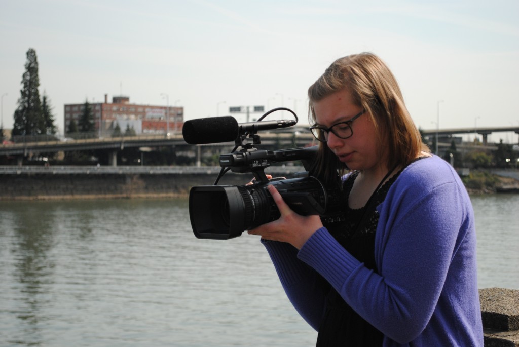 Student holding video camera along river