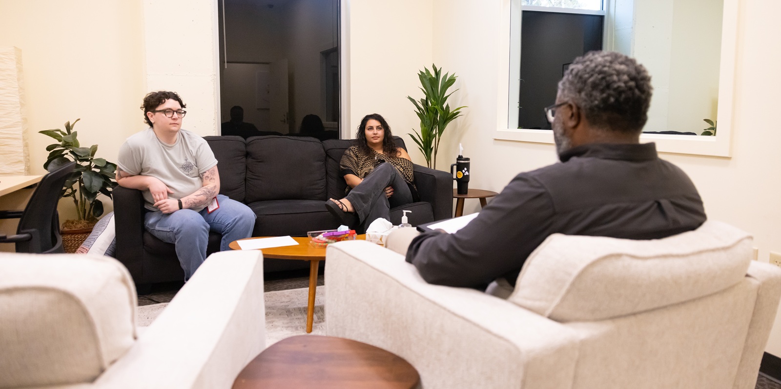 Professor Quantas Ginn leads his MFTH 522 course titled “Theory II” in role-play therapy simulations at The Couple and Family Therapy Center. The students sit on a grey couch facing the professor.